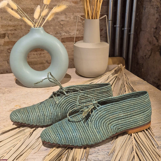 Zapato Aziza de Leke’s en rafia natural teñido en tono verde sobre hojas de palmera secas