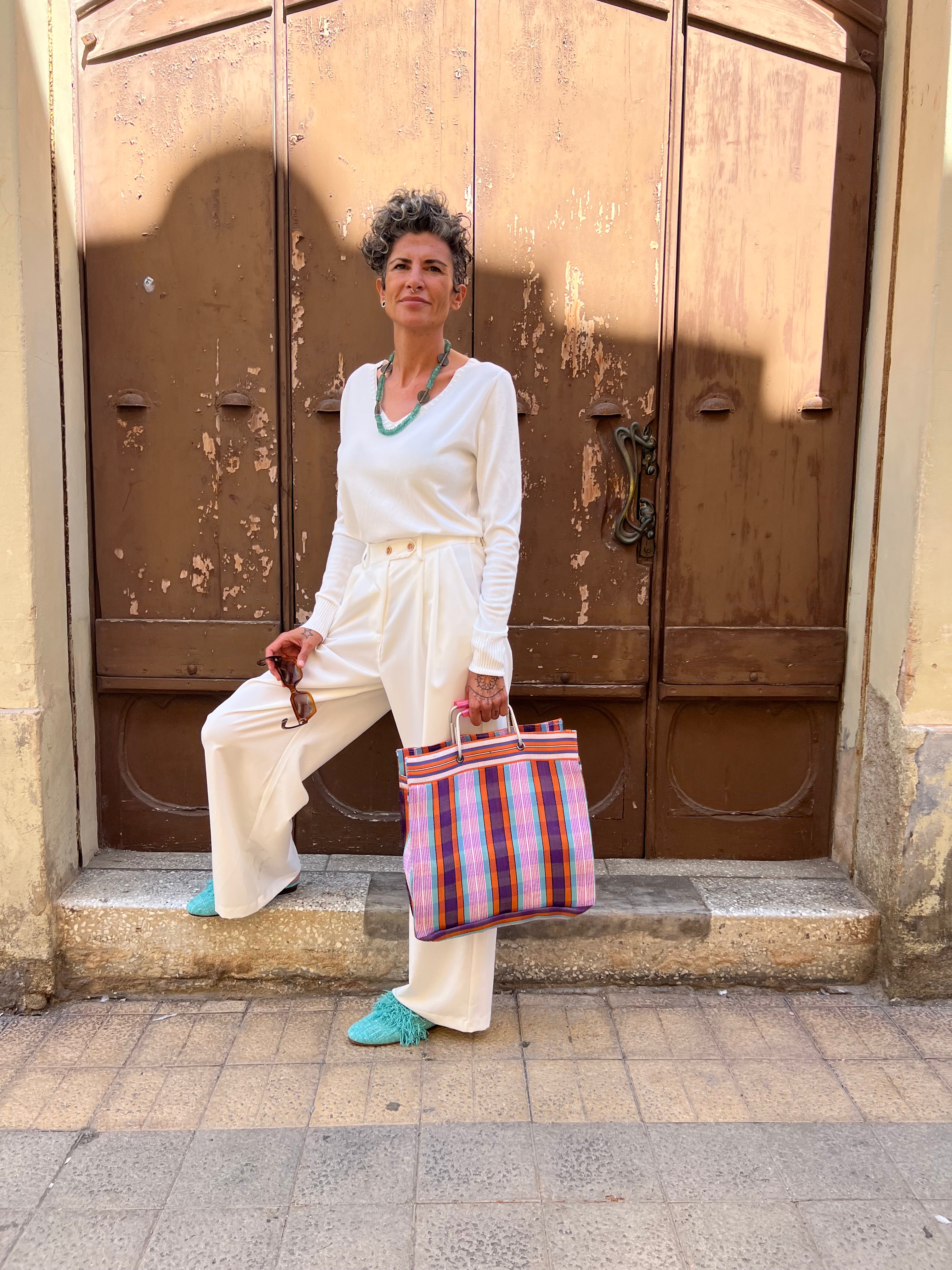 Mule Salma de Leke's con un outfit primaveral de pantalón palazzo blanco con jersey básico blanco y bolso market de nylon reciclado en tonos rosa, purpura y naranja